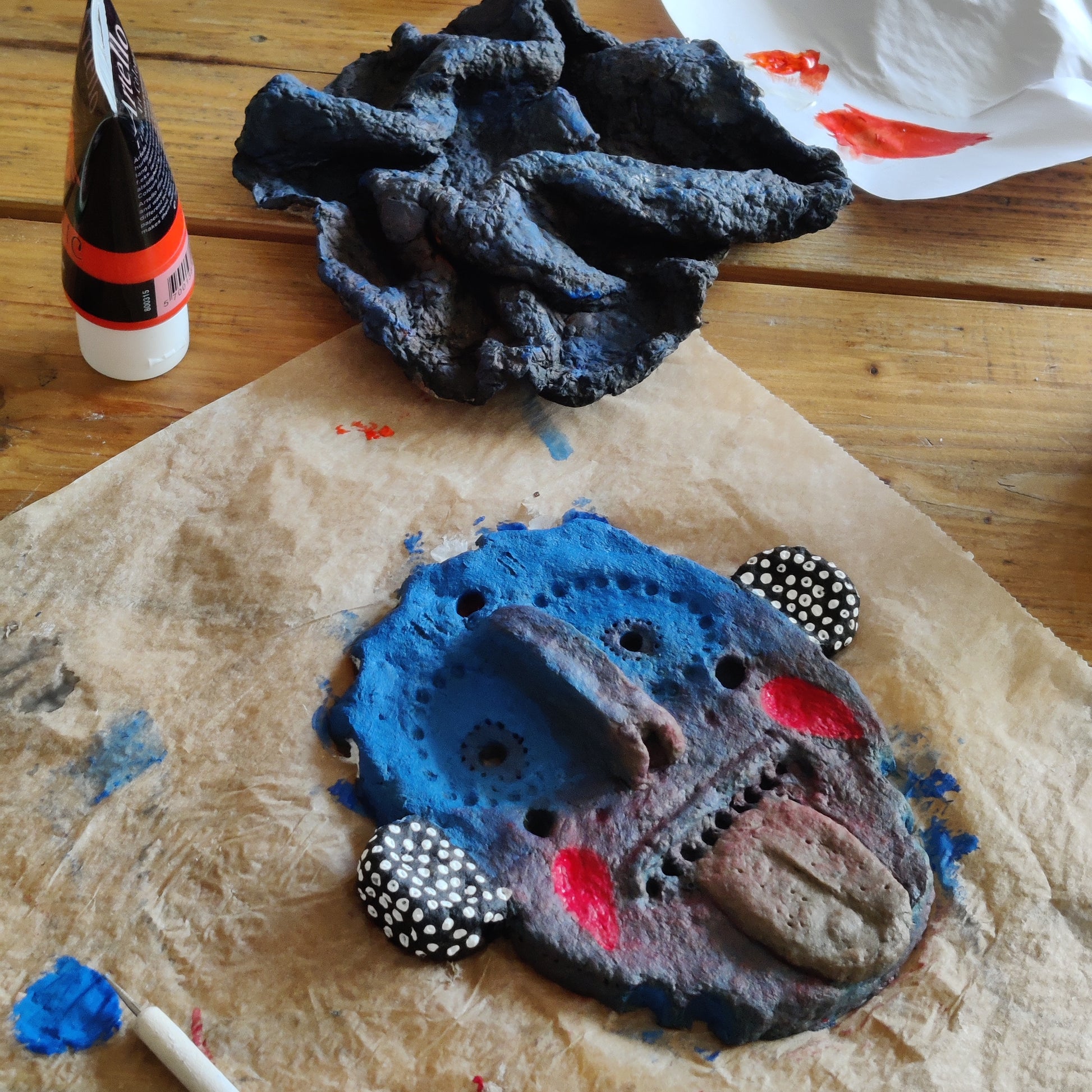 Artistic depiction of a face made from textured blue and gray material on a wooden surface with paint splashes.