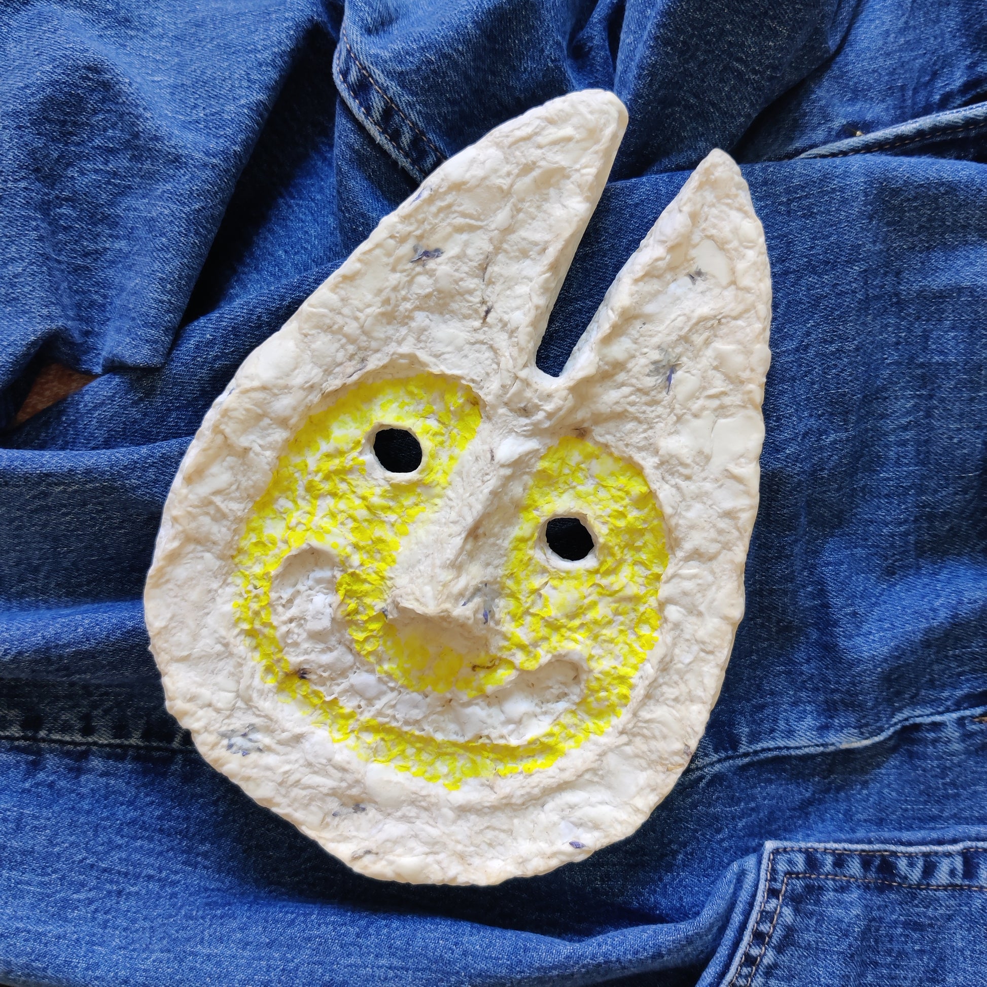 Decorative stone with a yellow symbol on a blue denim background -Rabbit Man handmade cardboard clay Mask